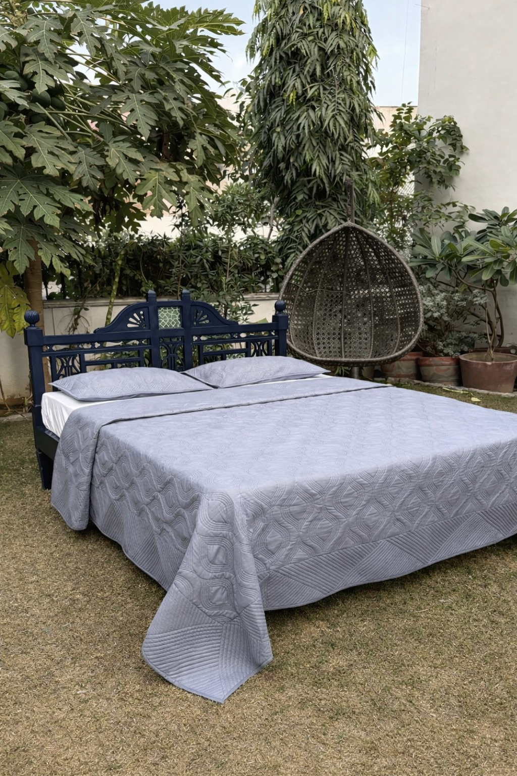 Light grey luxury quilted bedcover set displayed outdoors with navy blue headboard and textured geometric stitching