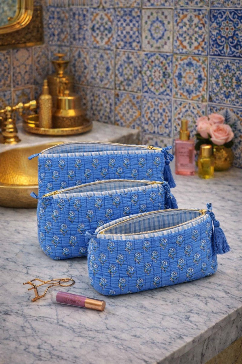 Blue quilted floral vanity pouch set with gold zipper and tassel, shown being zipped by hand on wooden table