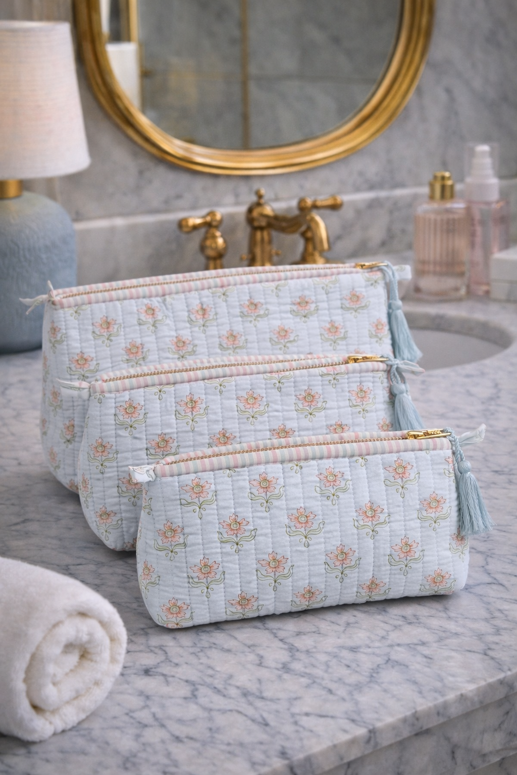 Blush lotus block print vanity pouch set in quilted cotton with tassels, elegant floral toiletry bags styled on marble counter.