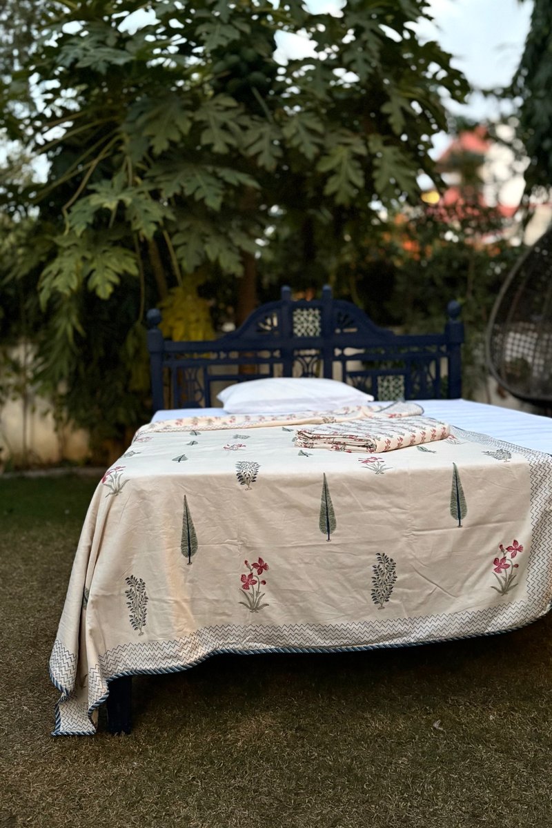 Beige hand block print cotton dohar with cypress tree and pink floral motifs styled on outdoor garden bed