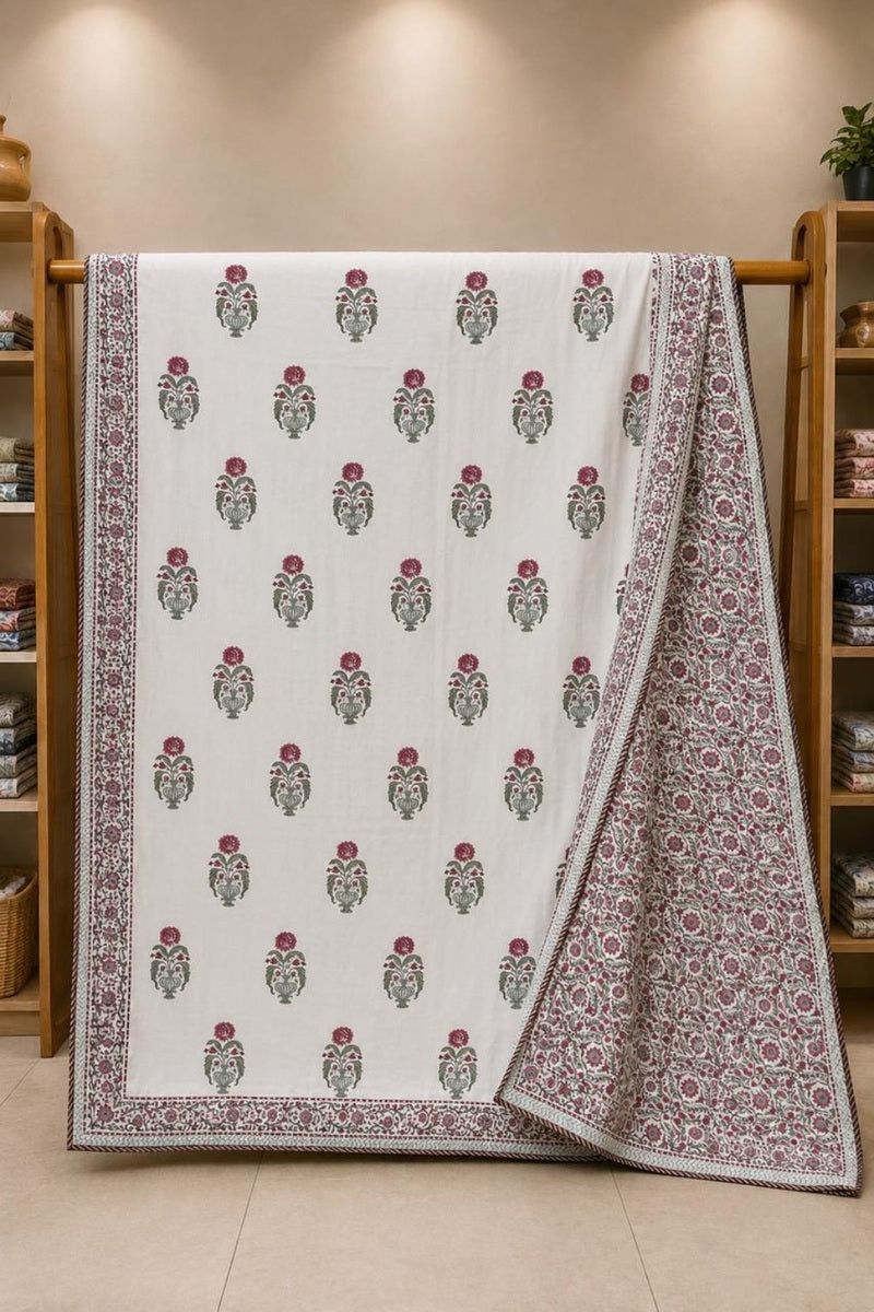 A white block-printed cotton Dohar, likely draped over a wooden rack in a showroom. The Dohar features a repeating floral motif in green and maroon, with a detailed maroon and green border.