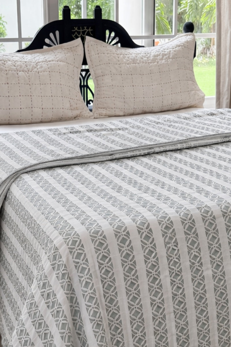 Bed with patterned bedding and pillows in a room with large windows.