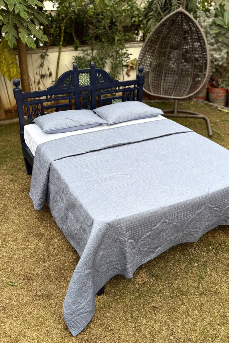 Luxury grey quilted bedspread with matching pillow shams displayed outdoors, showcasing detailed stitching and refined texture