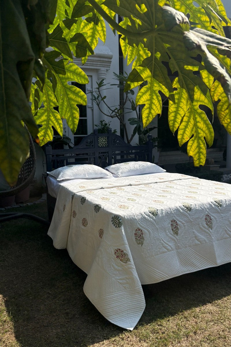Ivory cotton quilt with Mughal floral buta print and wave quilted texture in garden setting