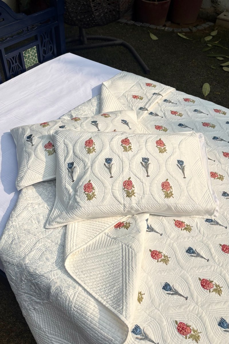 Gulnaar Garden hand quilted cotton bedspread in cream with floral block print, styled on outdoor bed