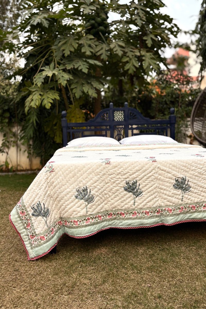 Reversible hand block printed quilt showing floral border and all-over print, draped on a bed in natural outdoor light