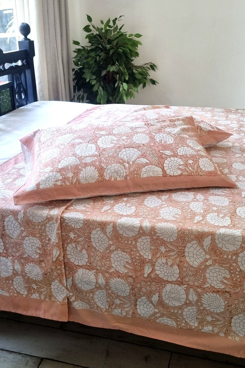 Peach hand block print cotton bedsheet set with white floral pattern and matching pillow covers
