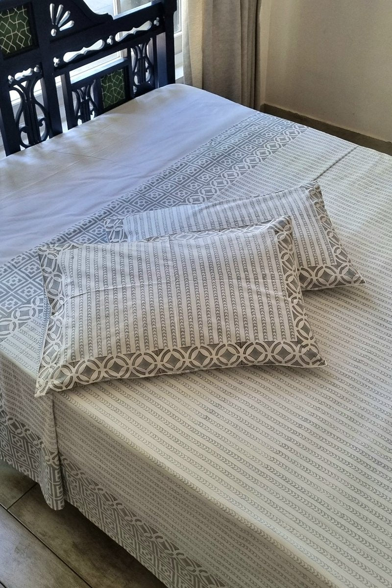 Grey and white hand block printed cotton bedsheet with geometric border design styled in sunlit bedroom