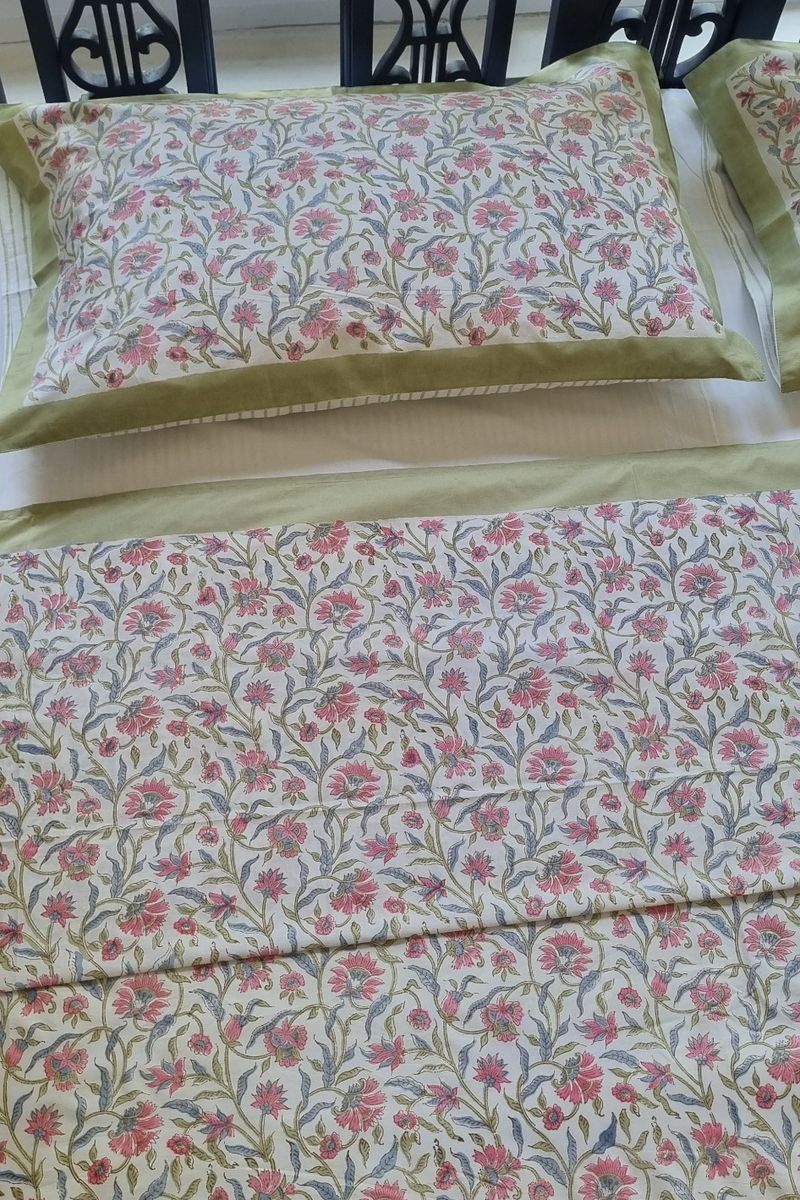 Pink and green floral hand block print cotton bedsheet with green border on wooden bed near large window