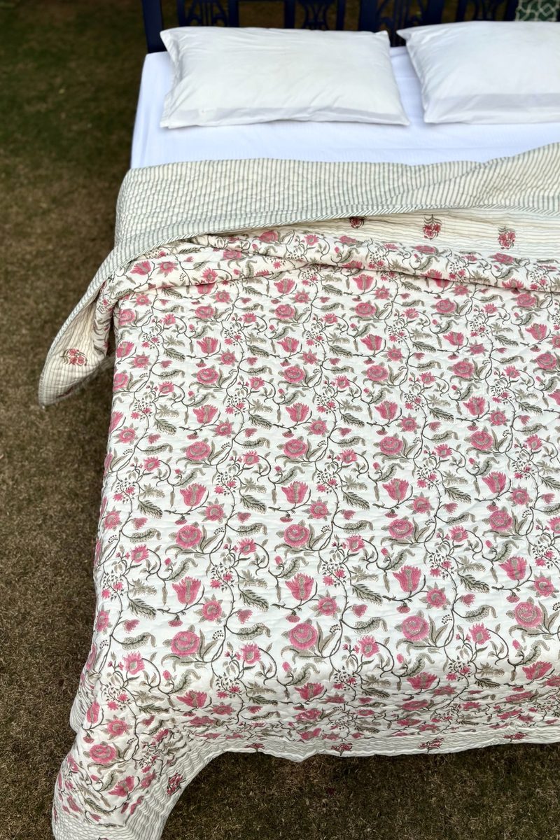 Traditional Jaal Bagh block print quilt featuring all-over pink floral motifs, displayed on a wooden bed in a garden setting
