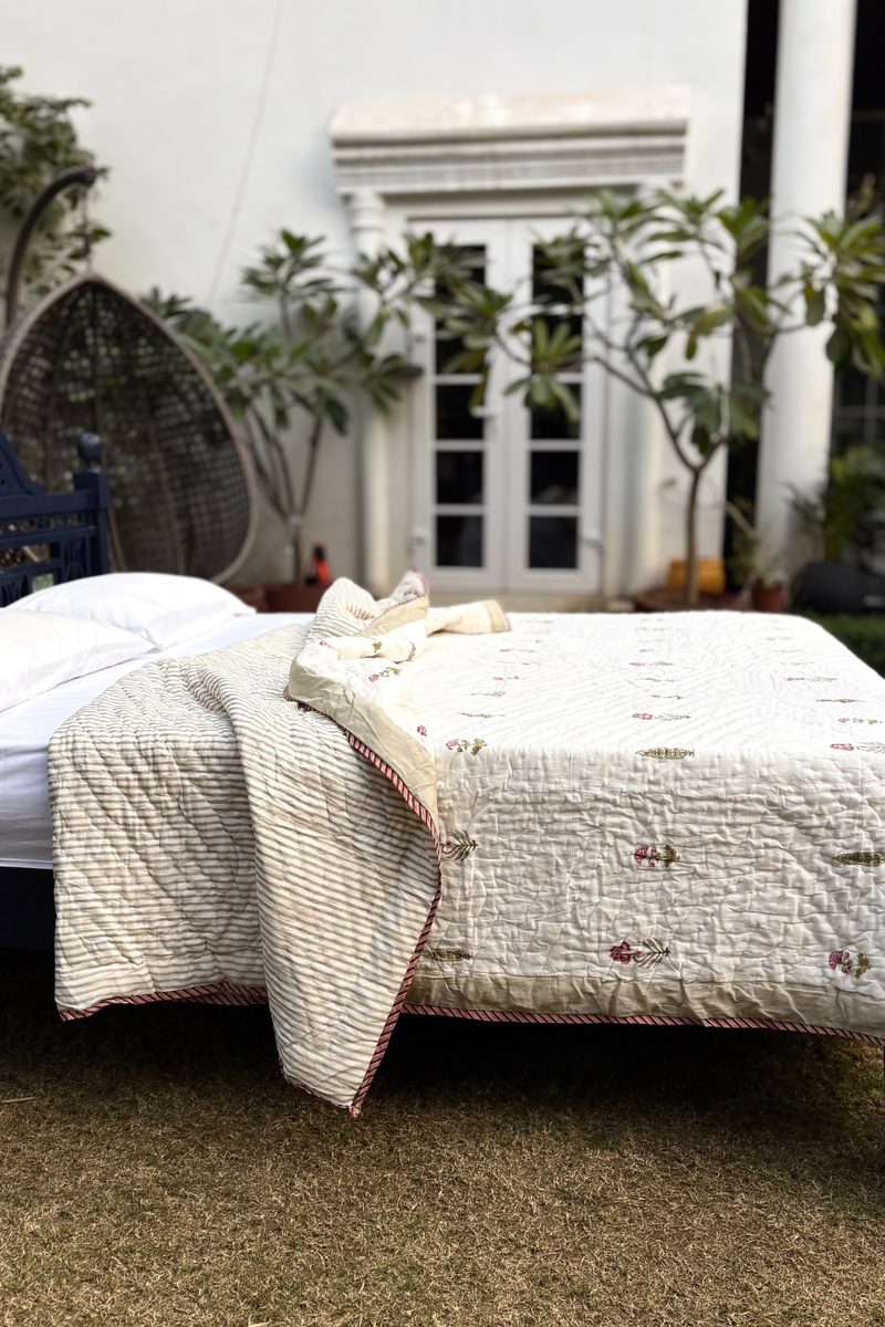Close-up of cream hand block printed quilt showing small floral motifs, quilted stitching and artisanal craftsmanship