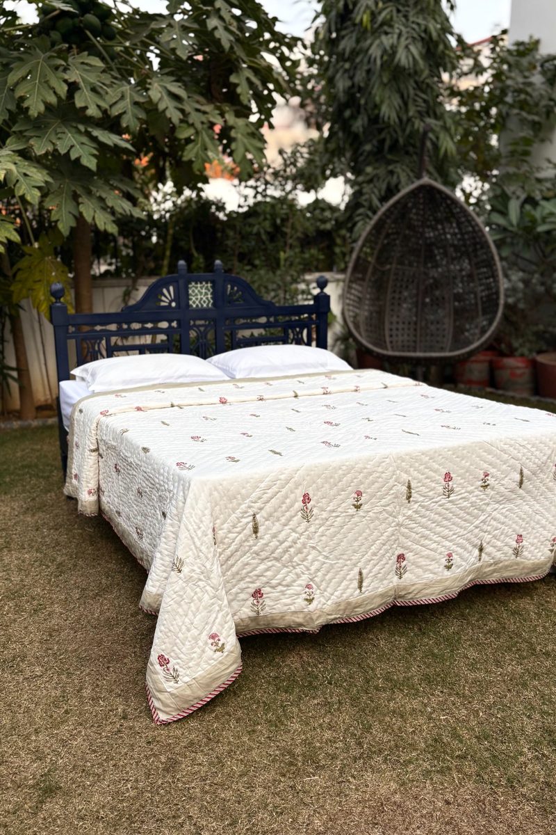 Hand block printed cream cotton quilt on wooden bed, delicate floral motifs with handcrafted Indian detailing in garden setting