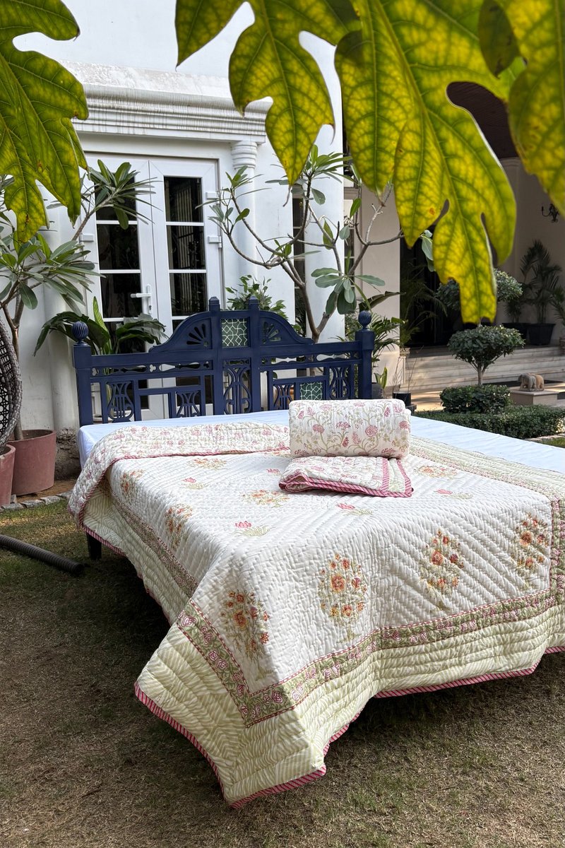 Hand block printed cream cotton quilt with pink tulip and floral bouquet motifs styled on a bed in garden setting