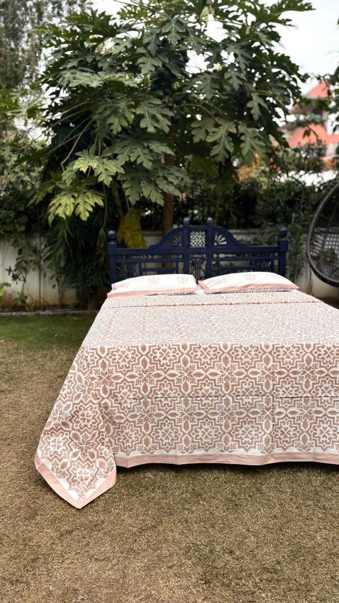 Blush jaal cotton bedsheet set with coordinated pillow covers styled on wooden bed in natural garden setting