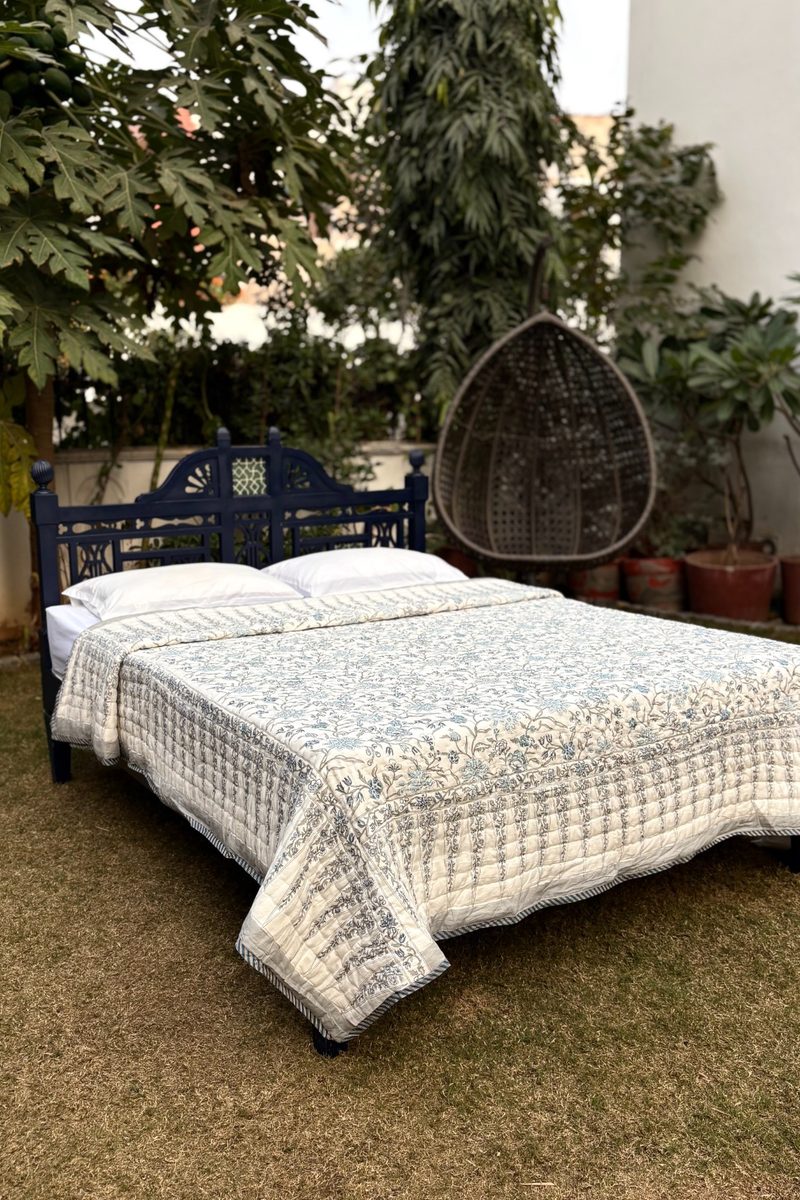 Hand block printed blue floral cotton quilt on wooden bed, artisanal Indian bedding styled in outdoor garden setting