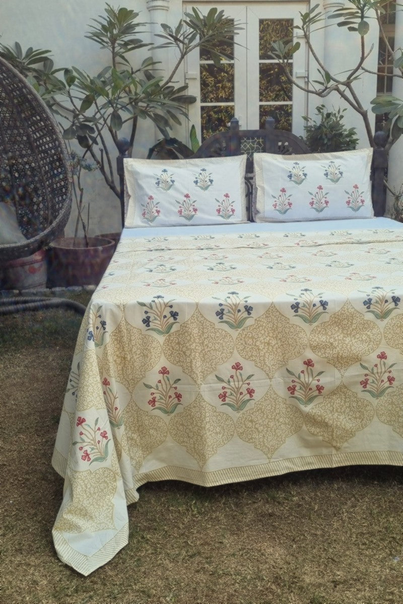 Hand block printed cotton bedsheet set with beige lattice pattern and red blue floral motifs styled on outdoor garden bed