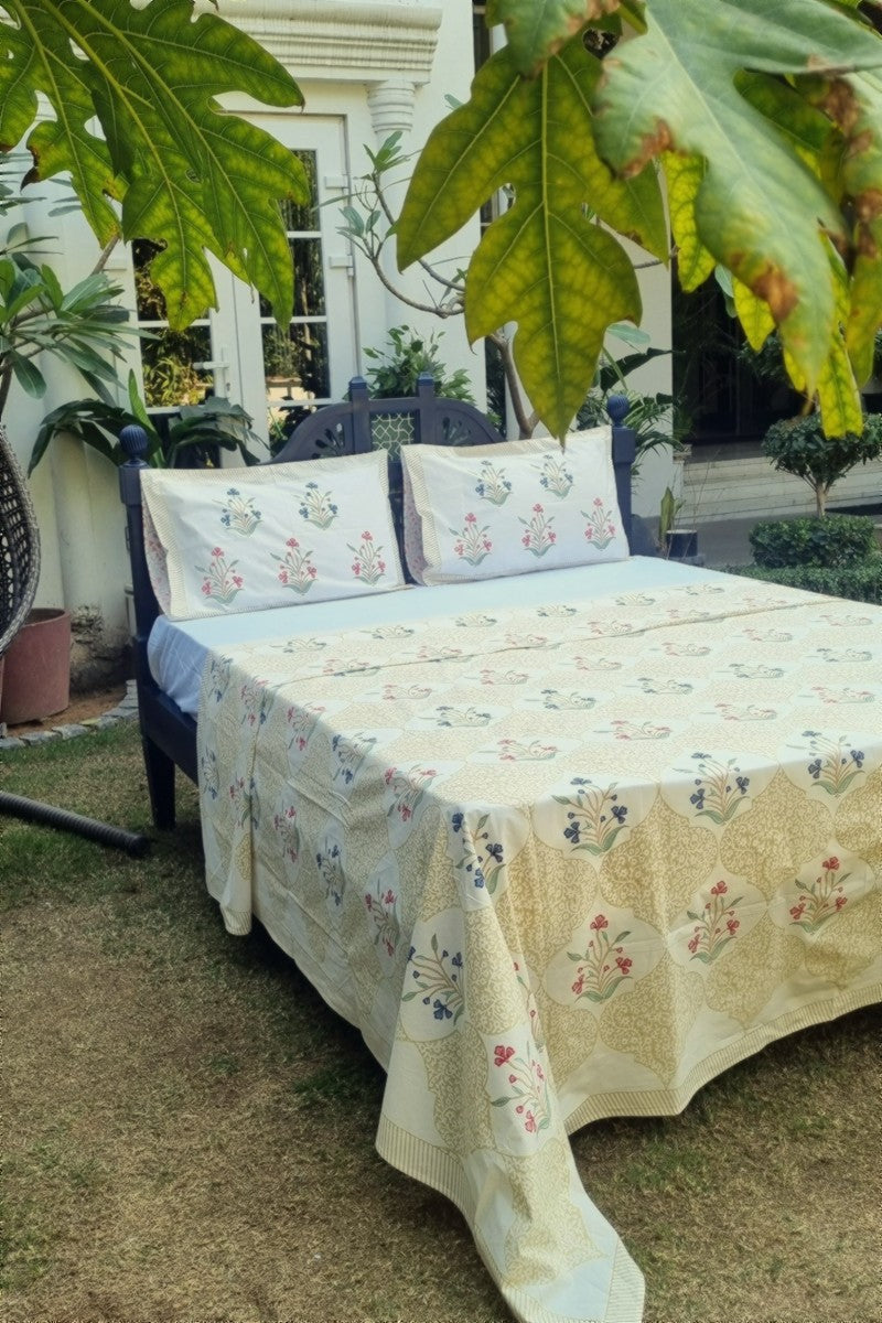 Beige Jaipuri block print bedsheet with scalloped lattice design and floral motifs photographed in natural garden setting