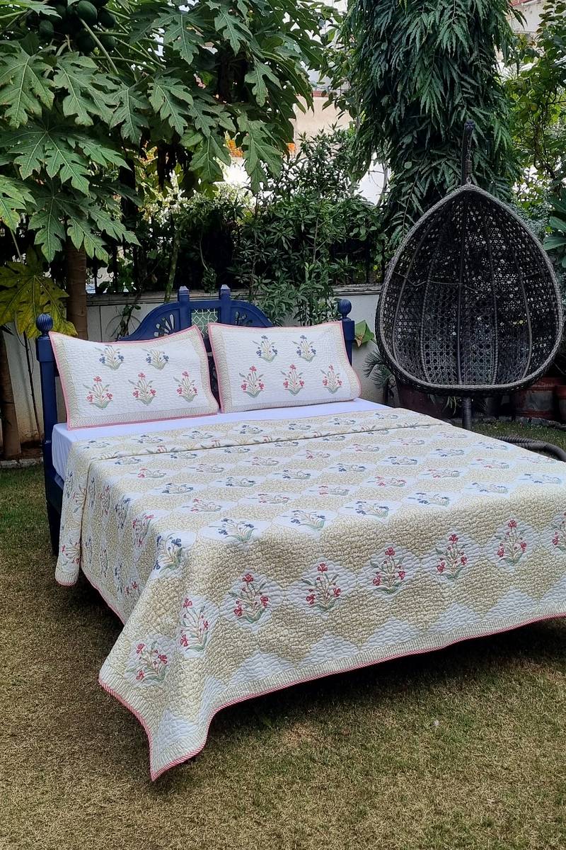 Hand block printed pastel floral cotton bedcover with ivory base and sage jaal pattern in garden setting