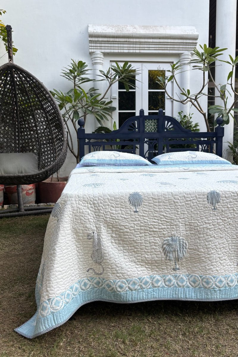 Soft quilted cotton bedspread in blue and white hand block print with matching pillow cover displayed on garden bed