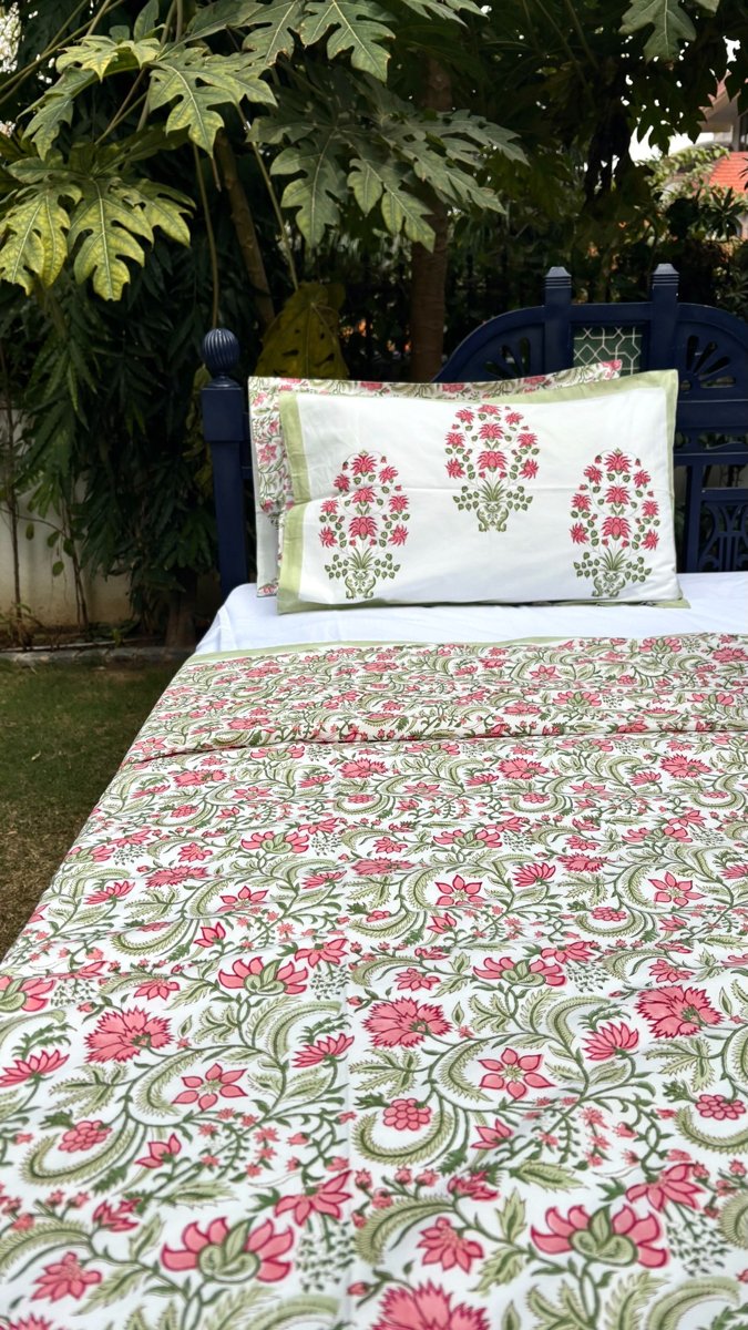 Pink and green floral jaal block print cotton bedsheet set displayed on wooden bed in garden setting