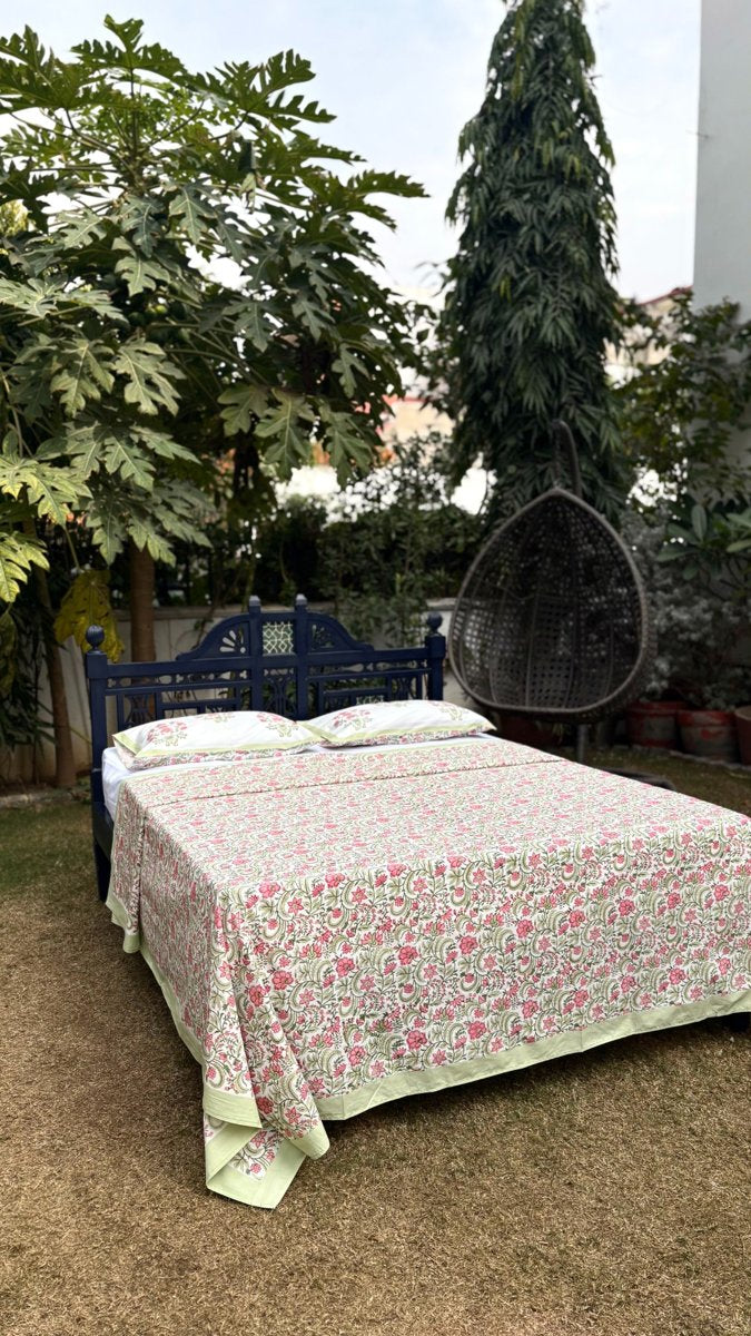Rose jaal handblock print cotton bedsheet with pink floral vine pattern and matching pillow covers styled outdoors