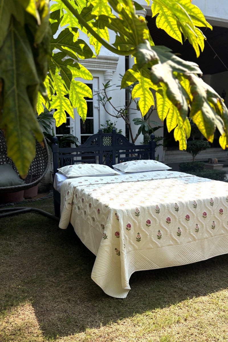 Cream cotton quilted bedcover with pink rose hand block print, luxury reversible floral quilt set displayed outdoors, king size bedding India