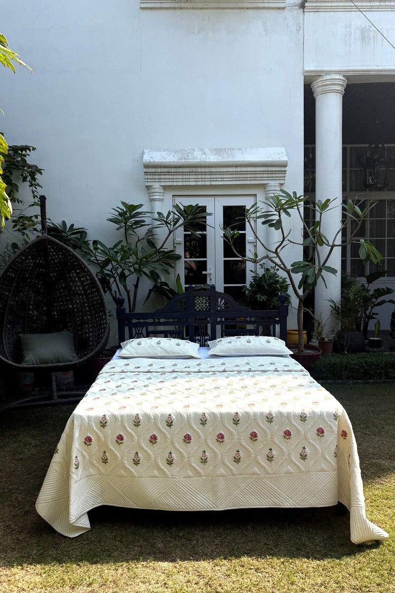 Hand block printed floral cotton quilt in cream with pink rose motifs, reversible quilted bedspread set styled in garden setting