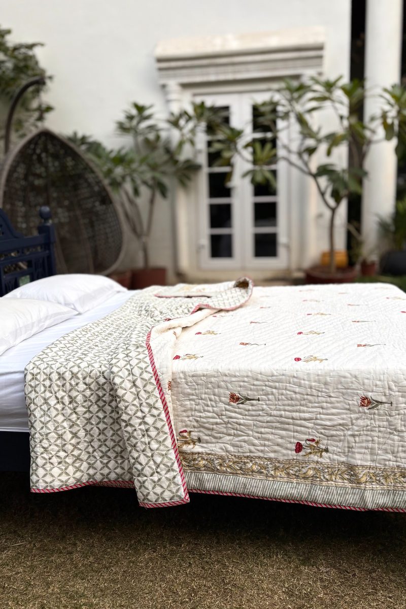 Reversible hand block printed quilt showing geometric reverse pattern and floral border, draped on a bed in natural light