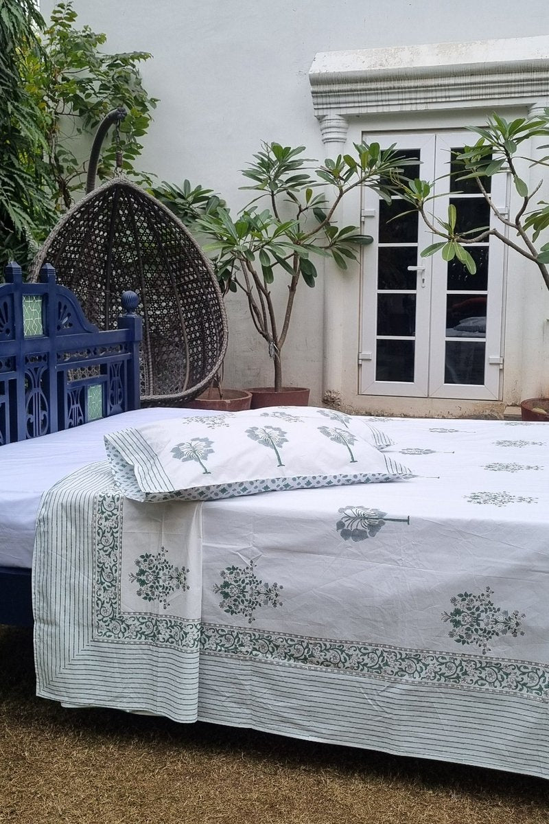 White cotton bedsheet with green tree buta handblock print and decorative border spread on traditional wooden bed