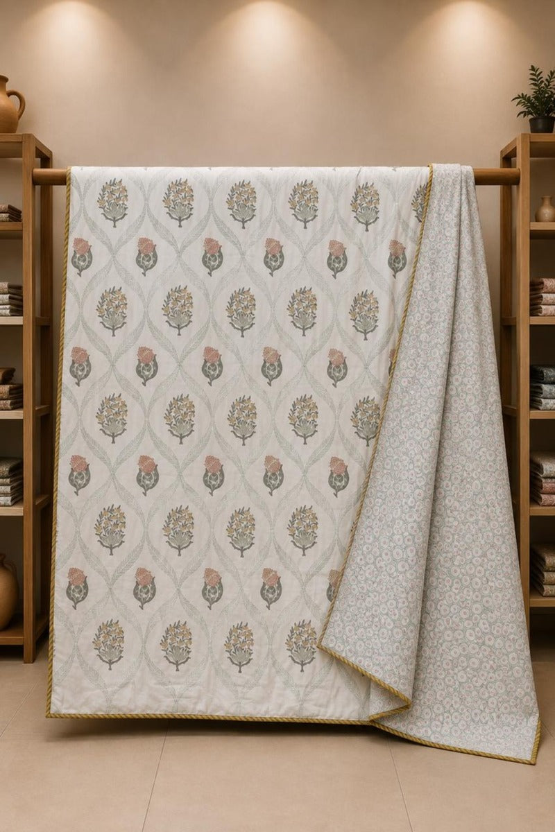 A cotton dohar with a repeating beige and muted pink floral pattern, draped over a wooden rack in a warm, neutral-toned room.