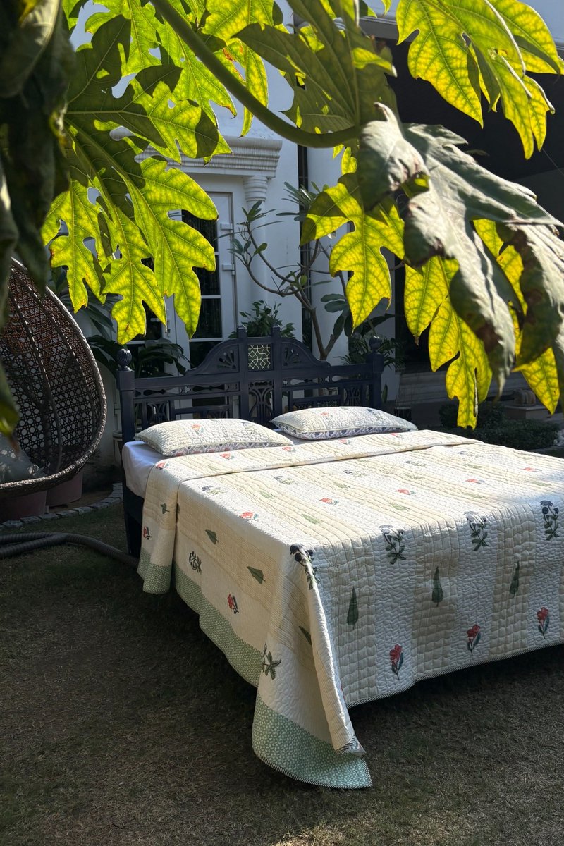 Hand block printed cotton quilt with floral and tree motifs, ivory reversible bedding set styled outdoors