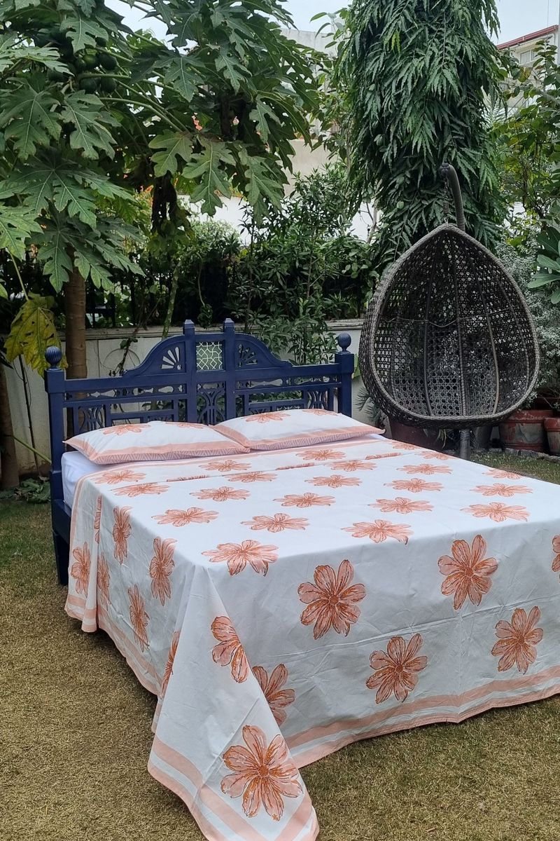 Peach floral hand block printed cotton bedsheet with matching pillow covers styled on wooden bed in outdoor garden setting