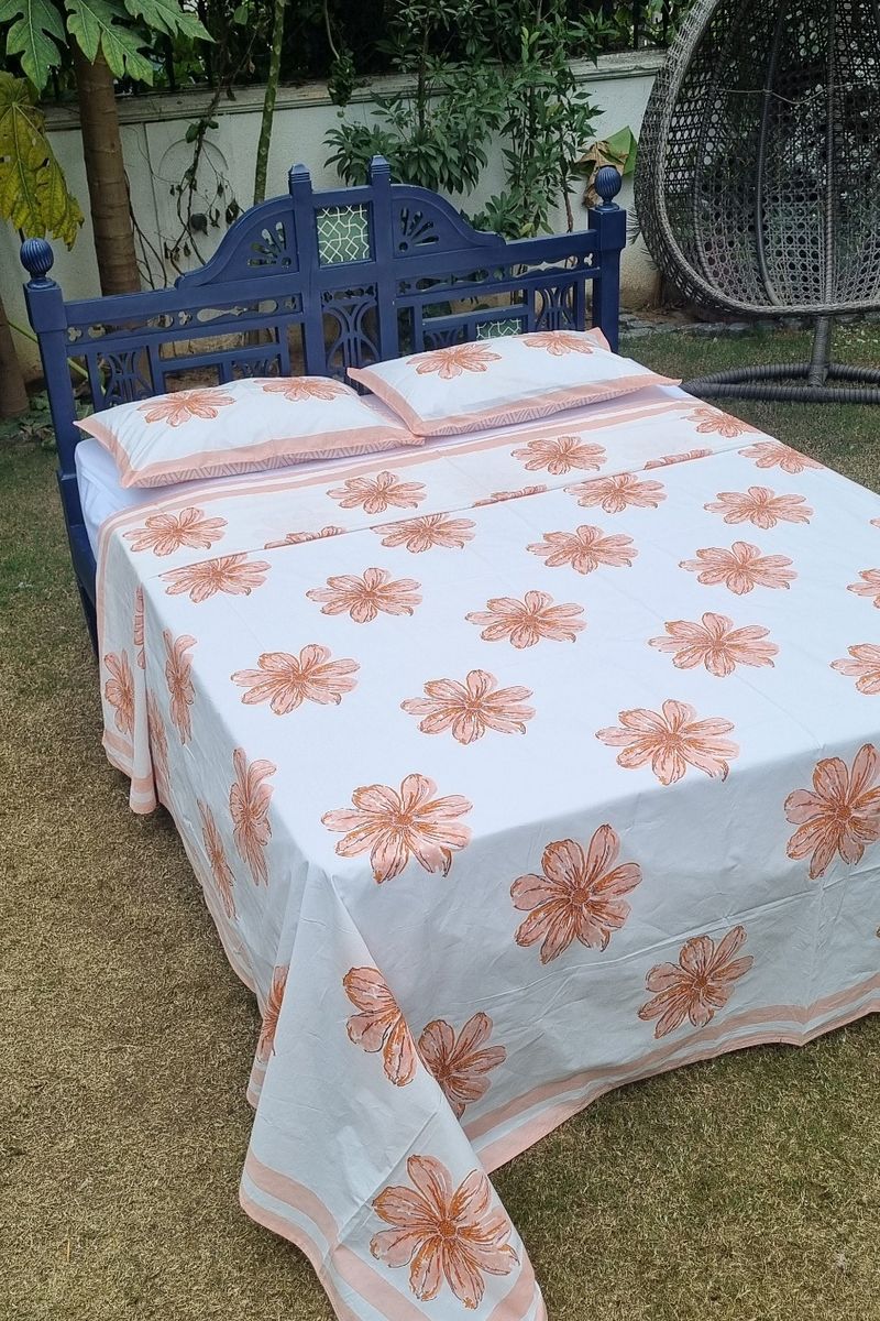 Hand block printed peach floral bedsheet with matching pillowcases on carved wooden bed