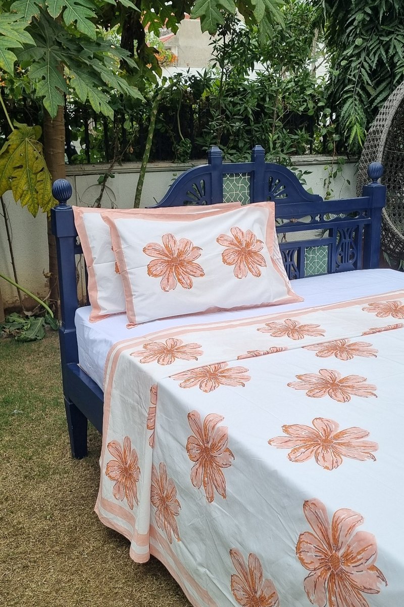 White cotton bedsheet with large peach flower block print and soft border detailing displayed on double bed