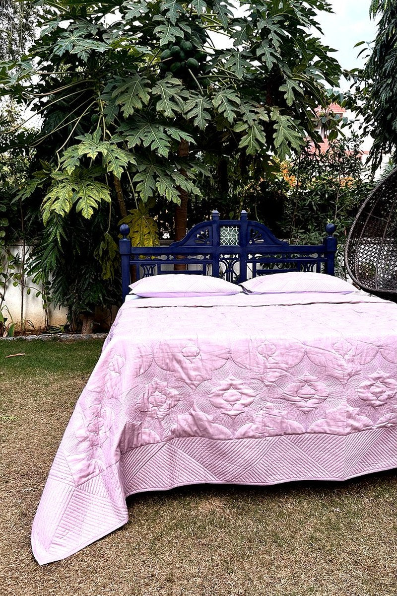 Blush pink hand-quilted cotton bedspread with geometric stitching, styled on an outdoor garden bed