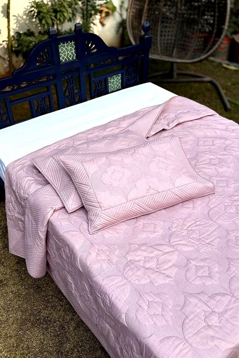 Close-up of blush pink quilt showing detailed hand quilting and textured stitch work on cotton fabric