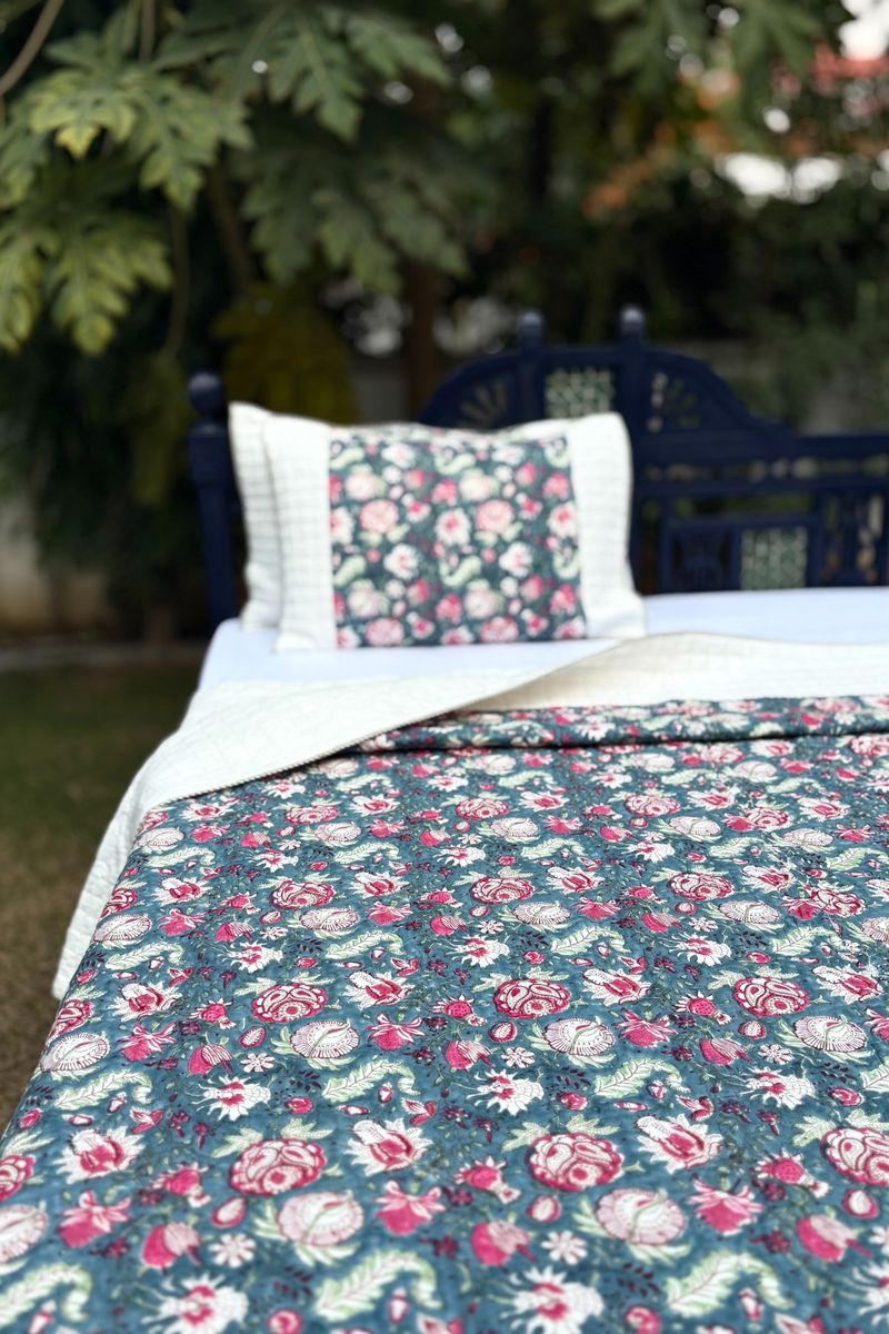 Hand block printed cotton quilt with floral pattern in teal and pink on outdoor wooden bed