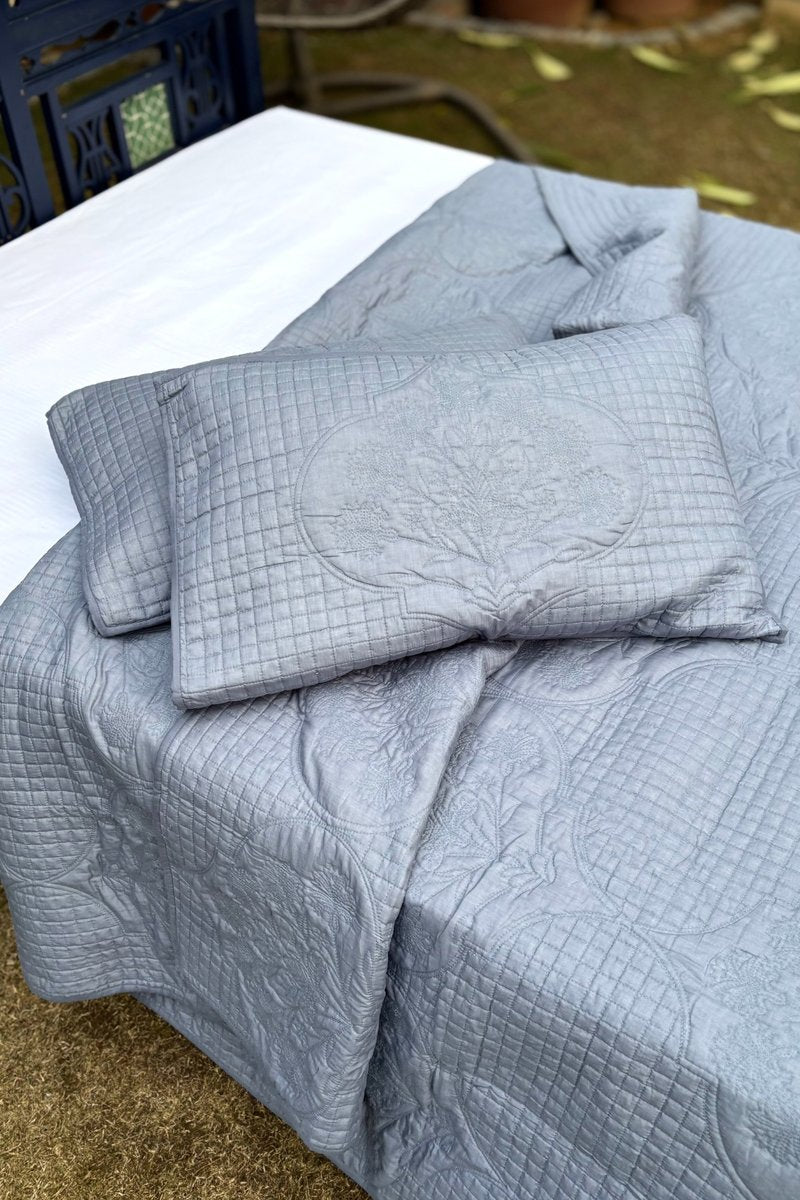 Grey quilted pillow sham with detailed stitched motif placed on bed, showcasing premium cotton fabric and elegant design