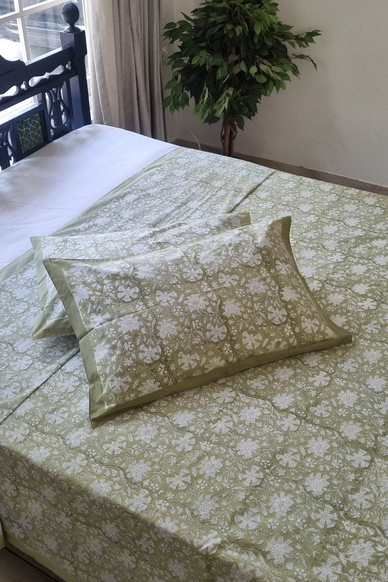 Sage green hand block print cotton bedsheet with white floral pattern and matching pillow covers styled in sunlit bedroom
