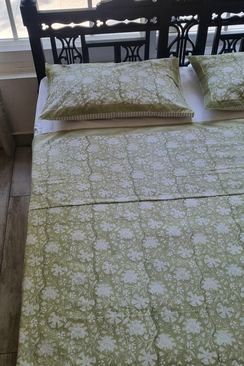 Close up of green floral hand block print cotton bedsheet fabric with matching pillow covers and border detail