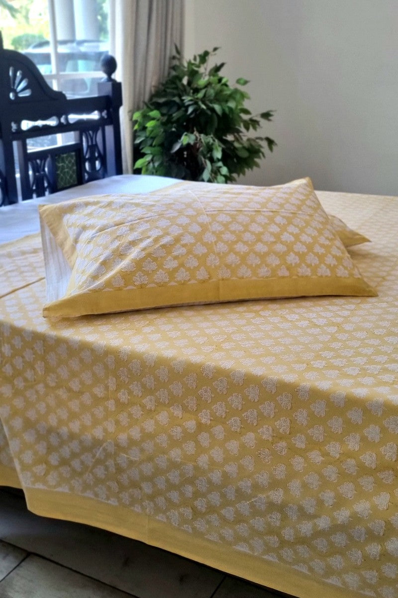 Soft yellow cotton double bedsheet set with white block print motif and two matching pillow covers near large window backdrop