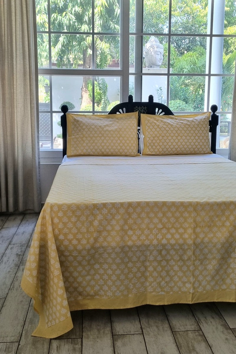 Yellow cotton bed linen set with small white block printed motifs styled on wooden bed in bright airy room
