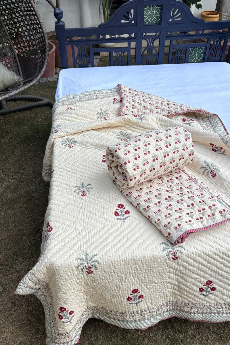 Premium ivory cotton quilt with red hand block floral print styled on bed in outdoor garden setting, reversible Quilt