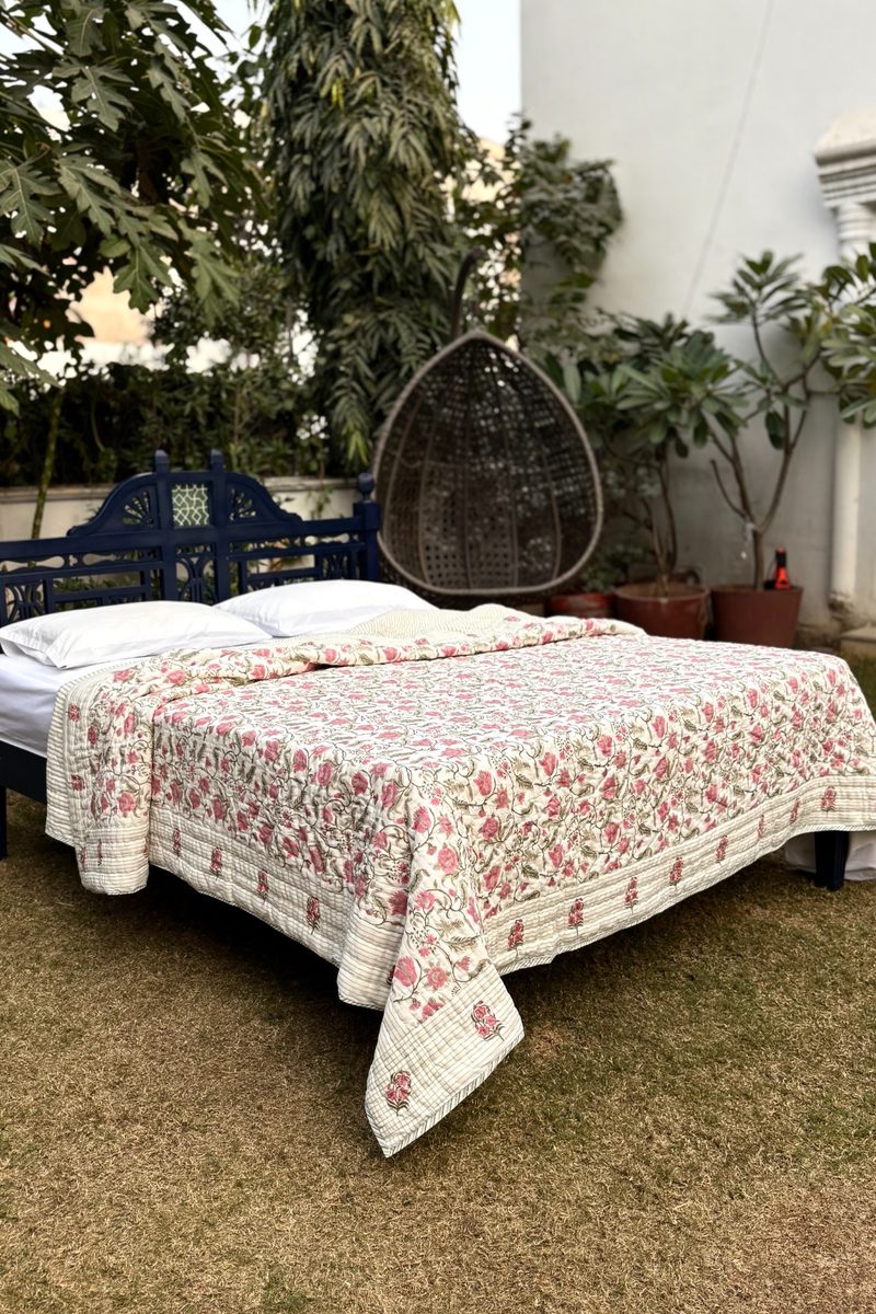 Jaal Bagh hand block printed cotton quilt with pink floral jaal pattern on a cream base, styled on a bed outdoors