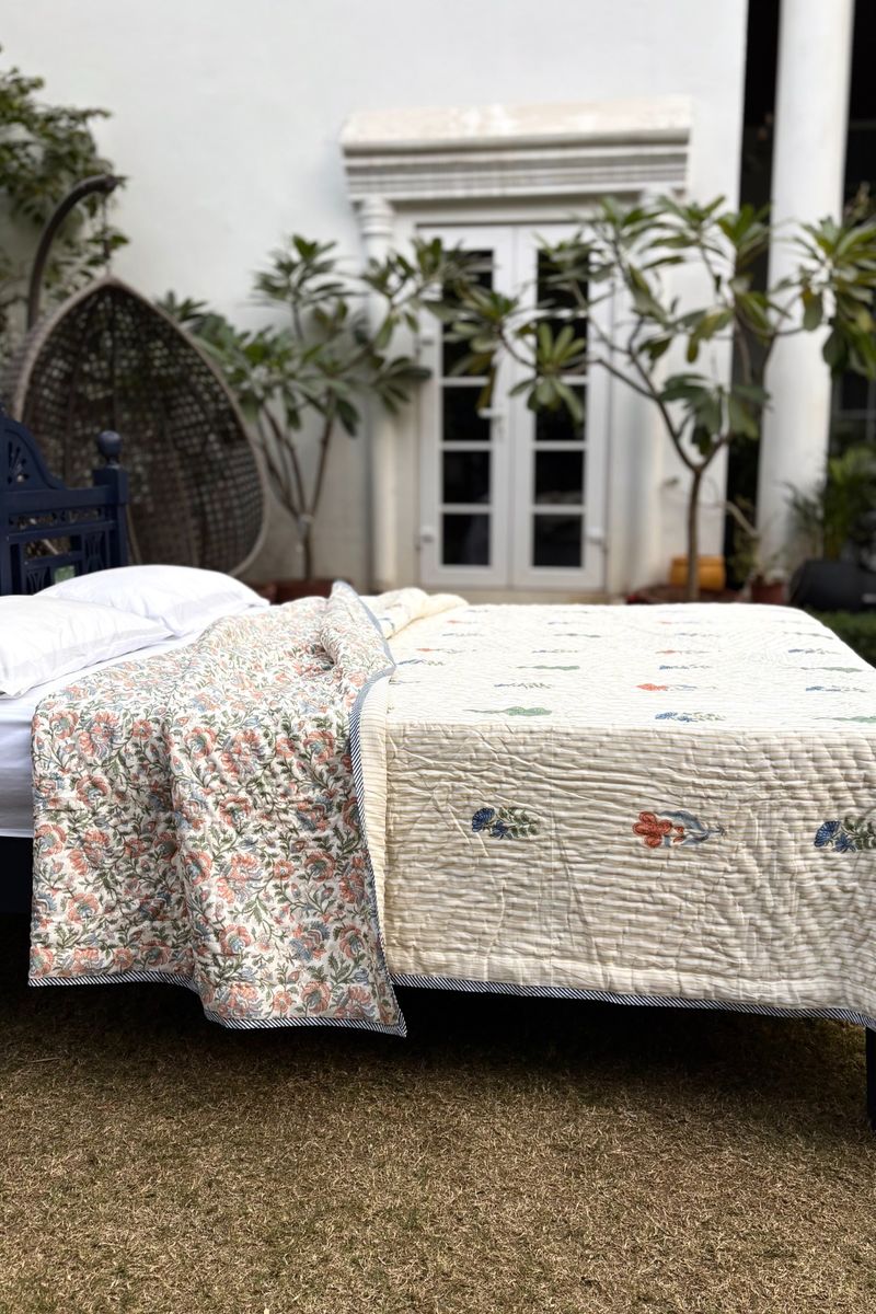 Lightweight cotton hand block printed quilt with floral motifs and striped texture, draped over a bed