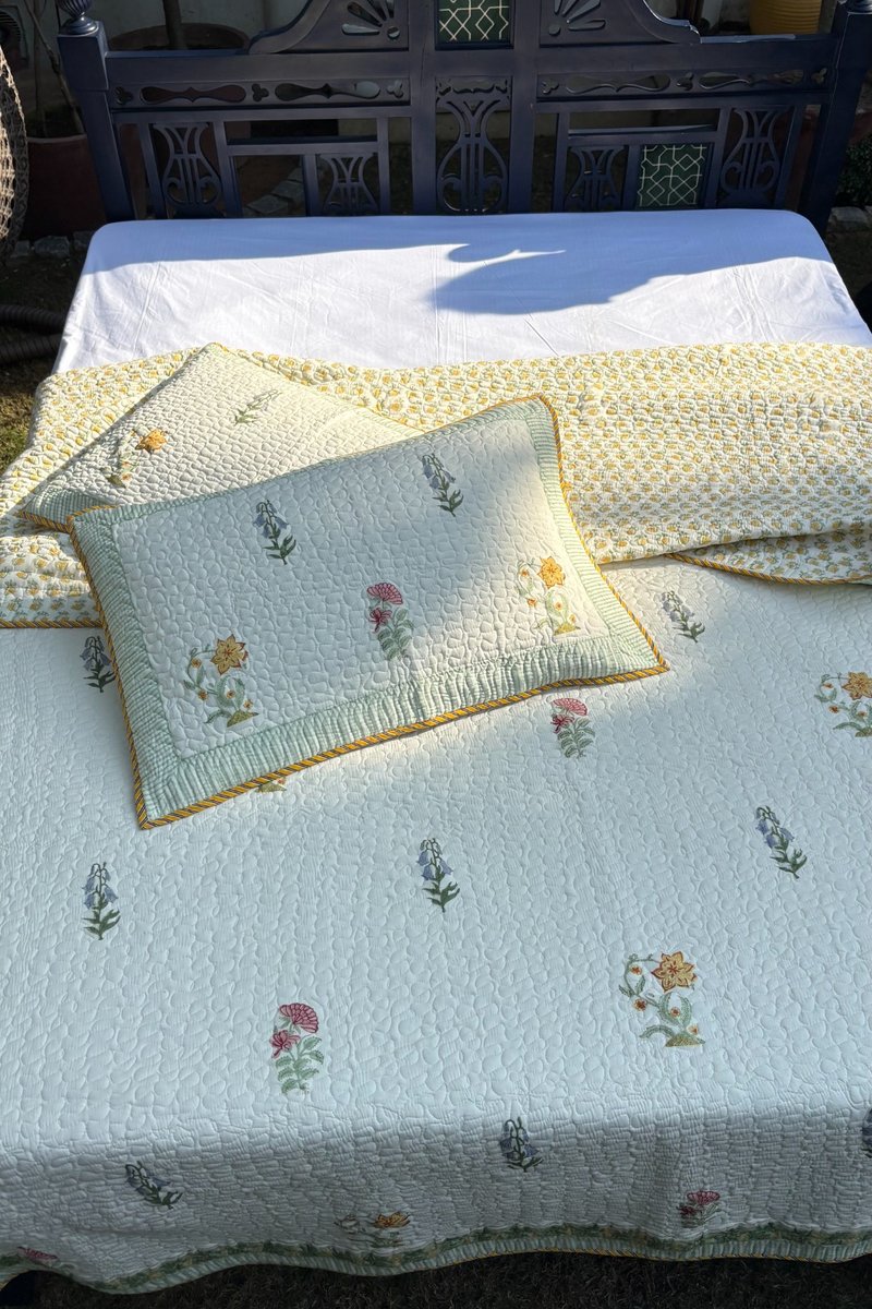 Ivory floral hand block print quilted bedcover with green border detail, premium cotton bedding set styled outdoors