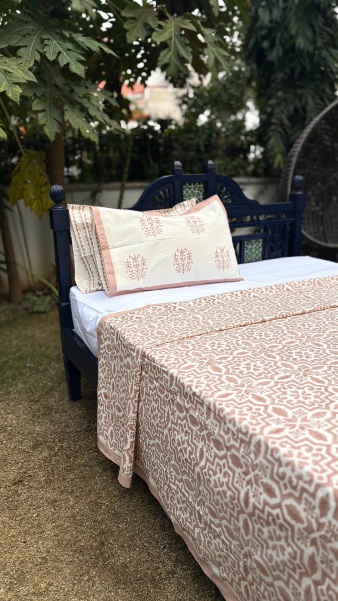 Soft blush geometric jaal print cotton bedsheet with matching pillow covers displayed on outdoor garden bed