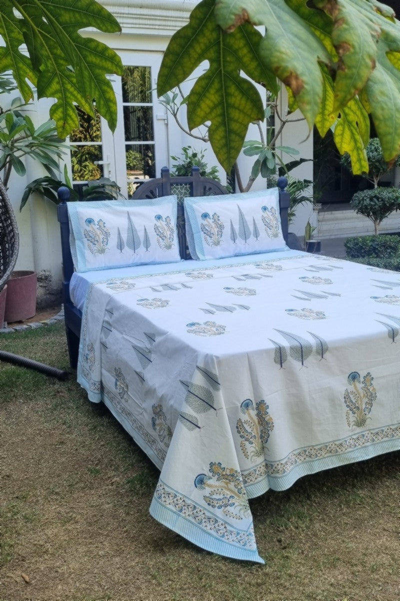 Hand block print cotton bedsheet set in aqua blue and soft green with floral buta and tree motif border styled outdoors in garden setting