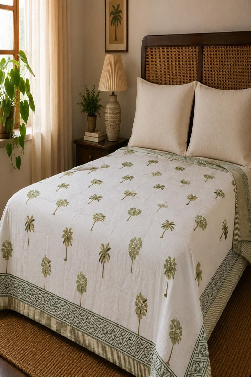A white Dohar with a green palm tree pattern and a decorative border, styled on a bed in a warm, sunlit bedroom.