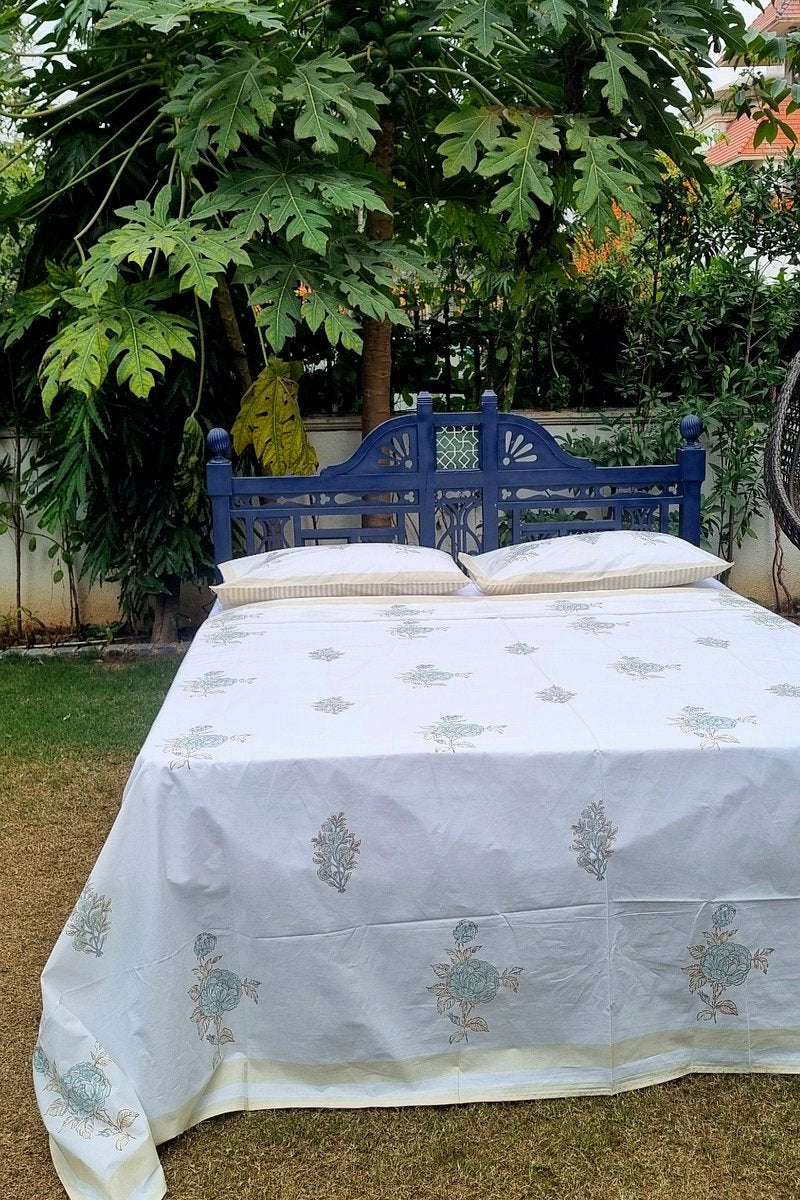 White cotton bedsheet with aqua floral block print and coordinated pillow covers styled on wooden bed in garden setting